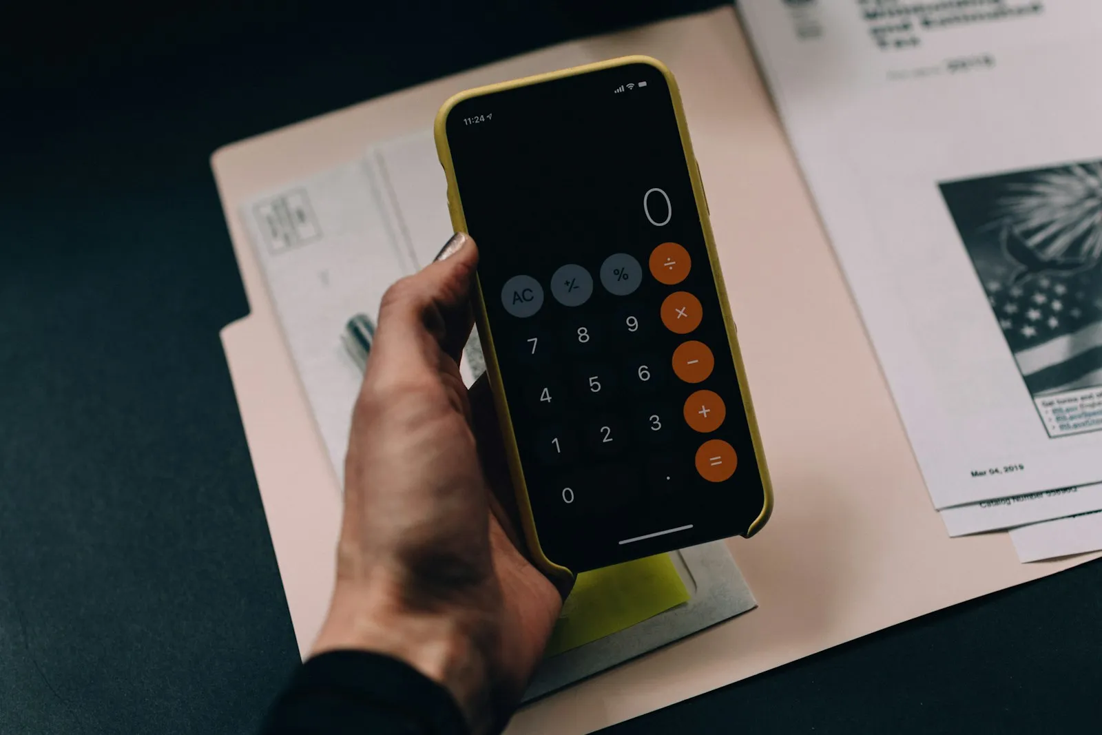 A hand checking a calculator beside bills and a notebook